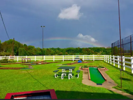 Mini golf course behind a white fence with a rainbow overhead